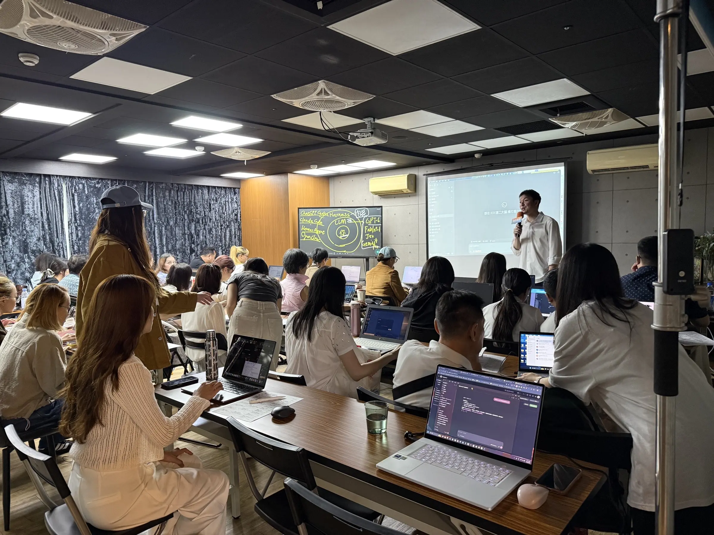 Podcast Space 上課實拍：講師拿著麥克風站在投影幕前，學員坐在長桌前用筆電跟著操作