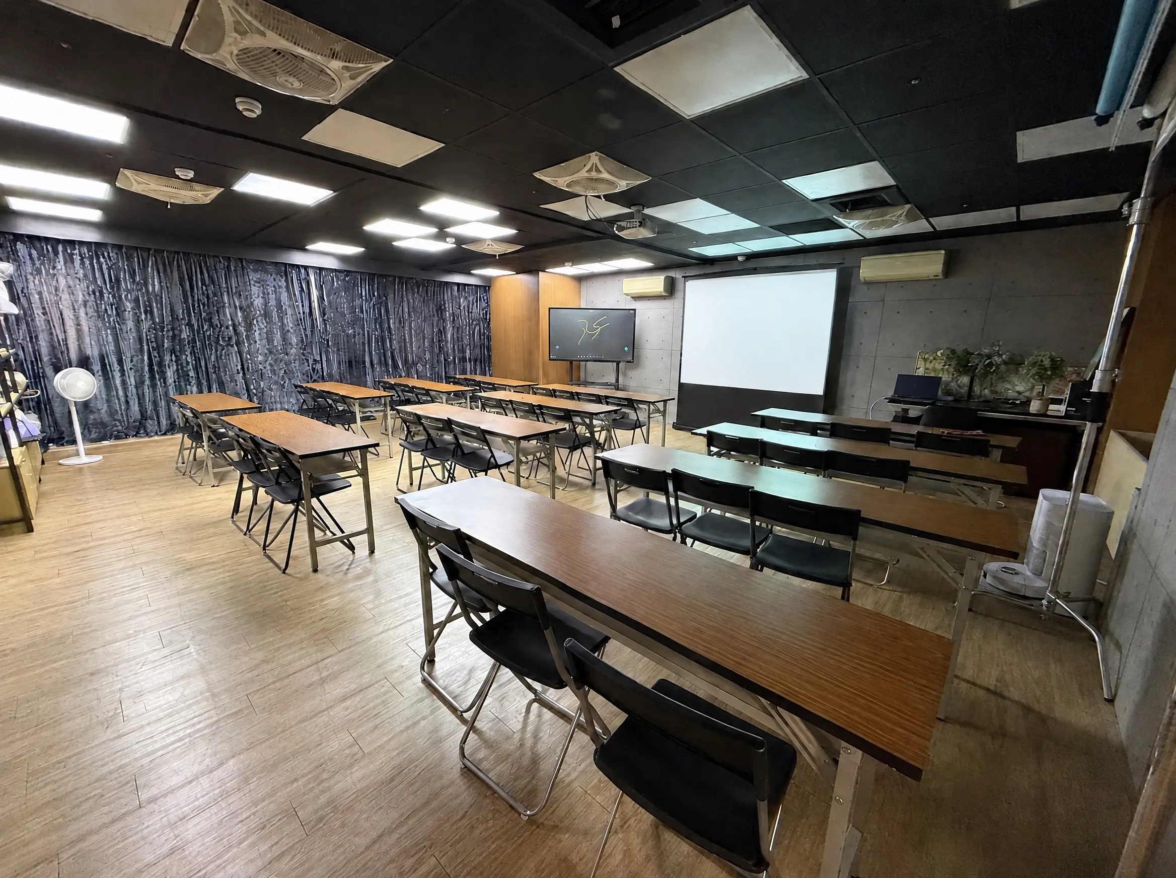 Podcast Space 排成教室的樣子：多排長桌與折疊椅面向投影幕，左側是大螢幕