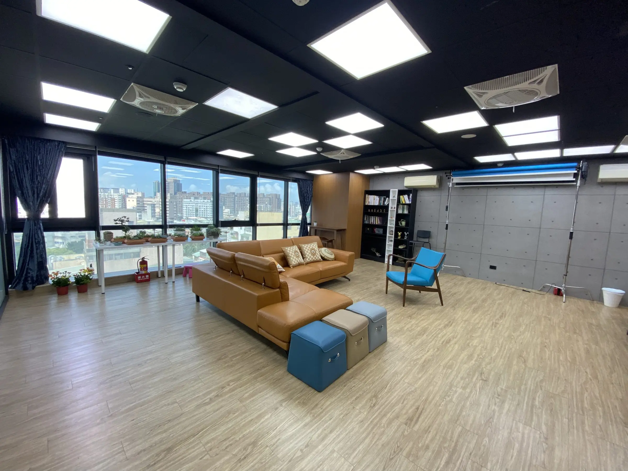 Podcast Space 現場實拍：落地窗旁的皮沙發區，右側是背景紙架與燈架